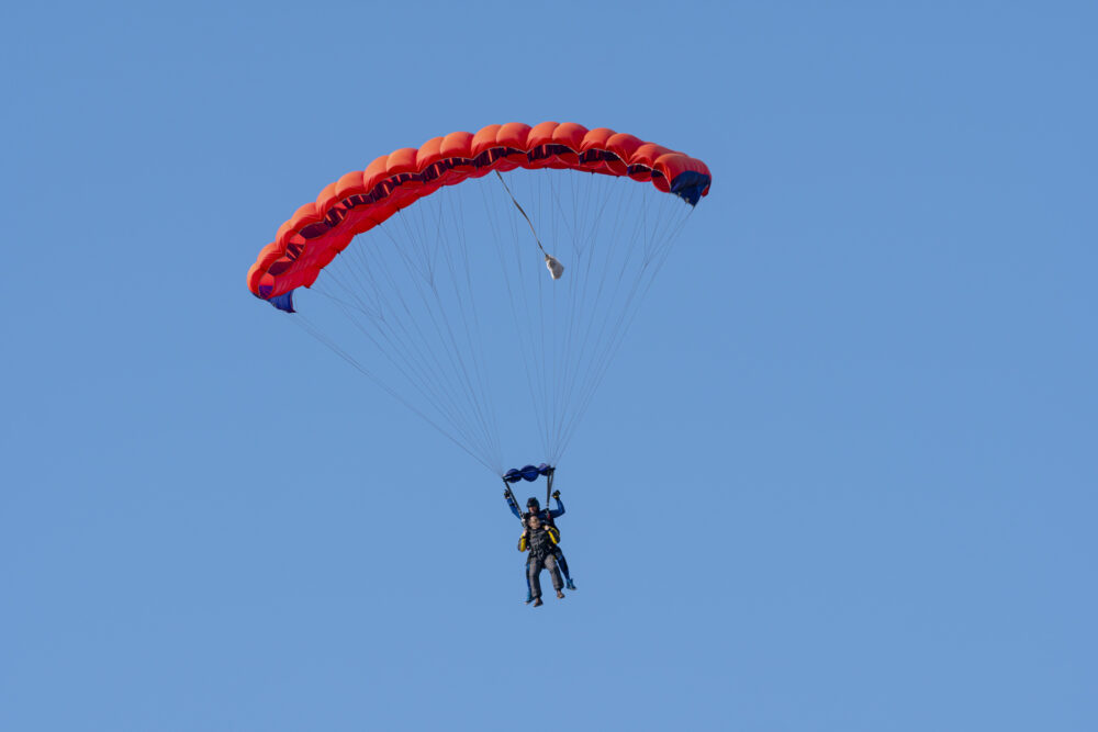 Tandem parachute jump. Silhouette of skydiver flying in blue clear sky. Concepts of extreme sport and adrenaline.