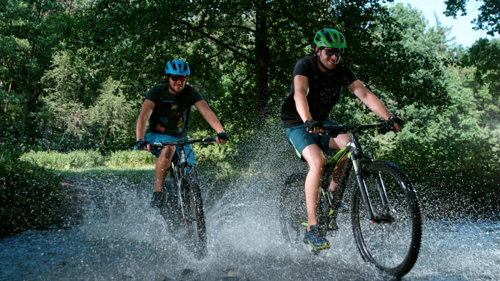 Freeze motion of sportsmen riding bicycles in the shallow stream and splashing water.