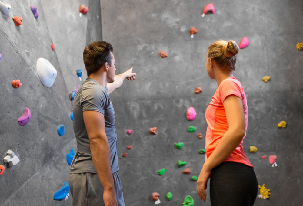 fitness, extreme sport and bouldering concept - man and woman exercising at indoor climbing gym