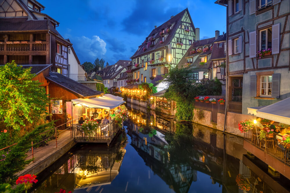 Colmar, France. Half-timbered houses and verandas of restaurants reflecting in the water at dusk in Petite Venise area