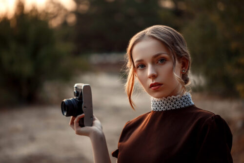close-up portrait of a young beautiful girl in a brown dress in a retro style with a vintage camera in her hands on an abandoned road.